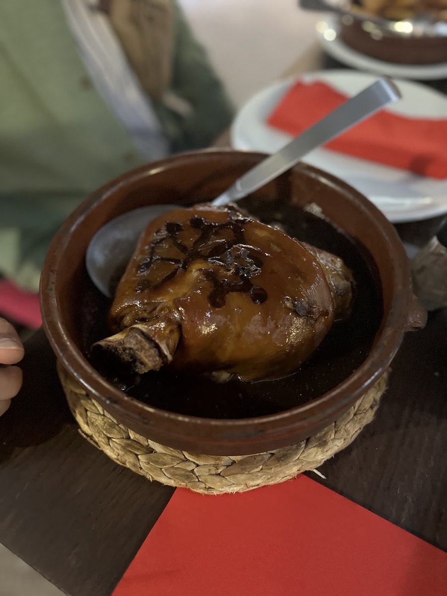 Pièce de viande confite au four dans une cassole en terre cuite, sur son dessous-de-plat en paille.