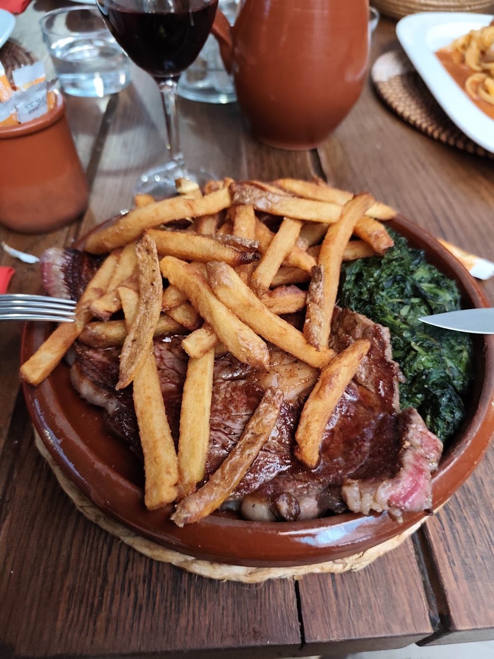 Entrecôte grillée recouverte de frites maison, servie dans une cassole.