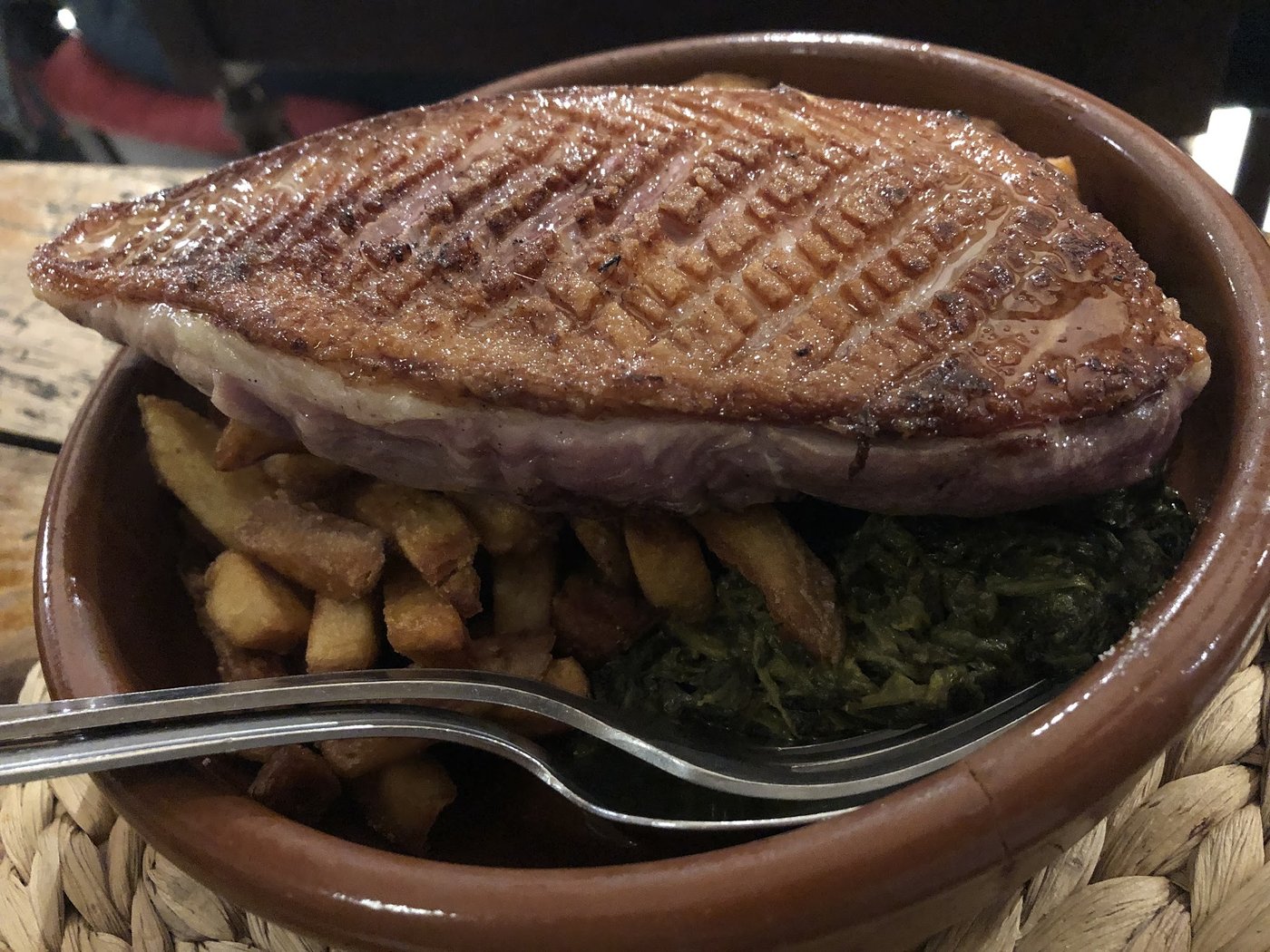 Magret de canard grillé, peau quadrillée, posé sur des frites maison dans une cassole.