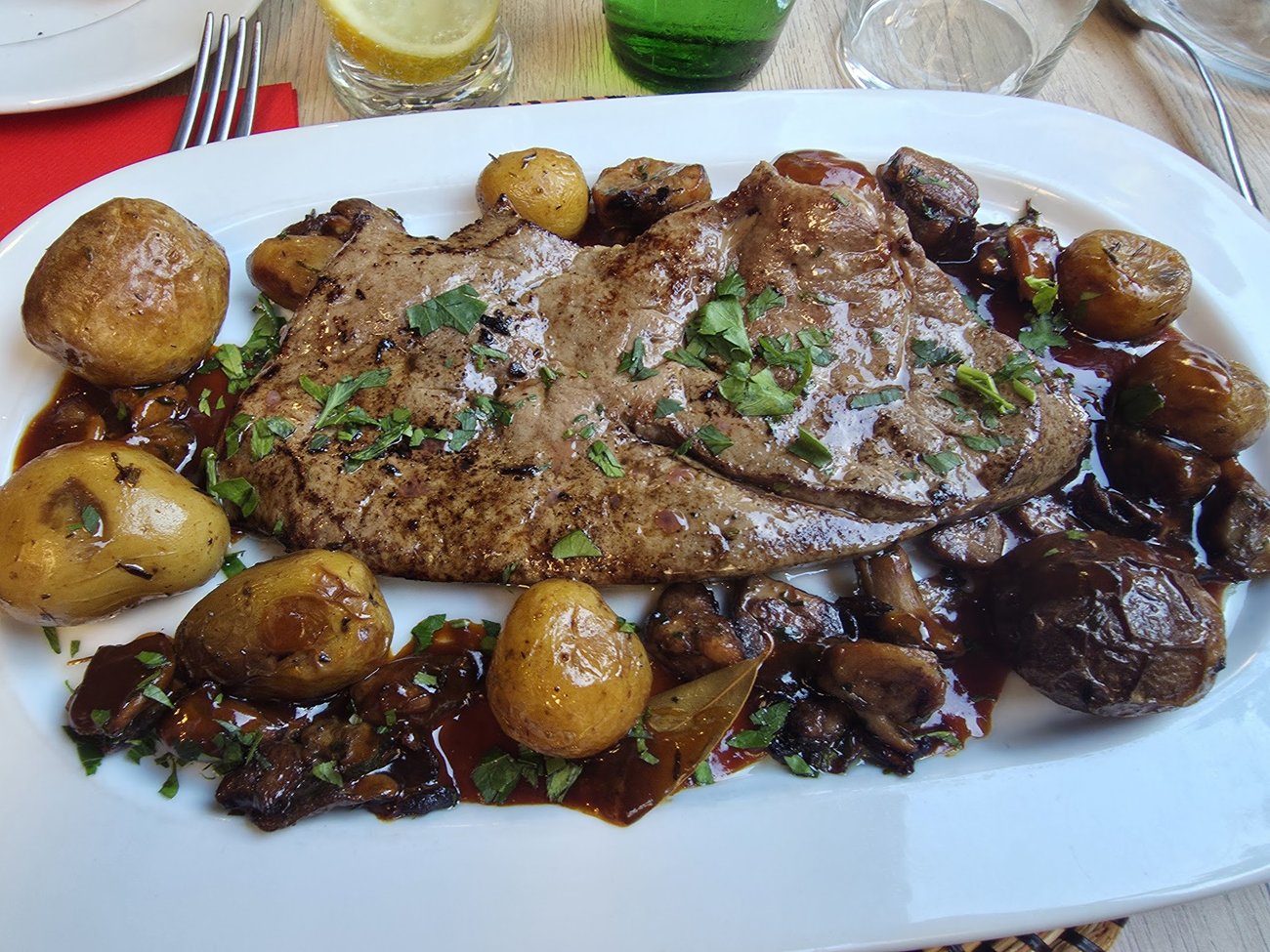 Tranches de viande aux cèpes et pommes grenailles, jus corsé, sur plat blanc.